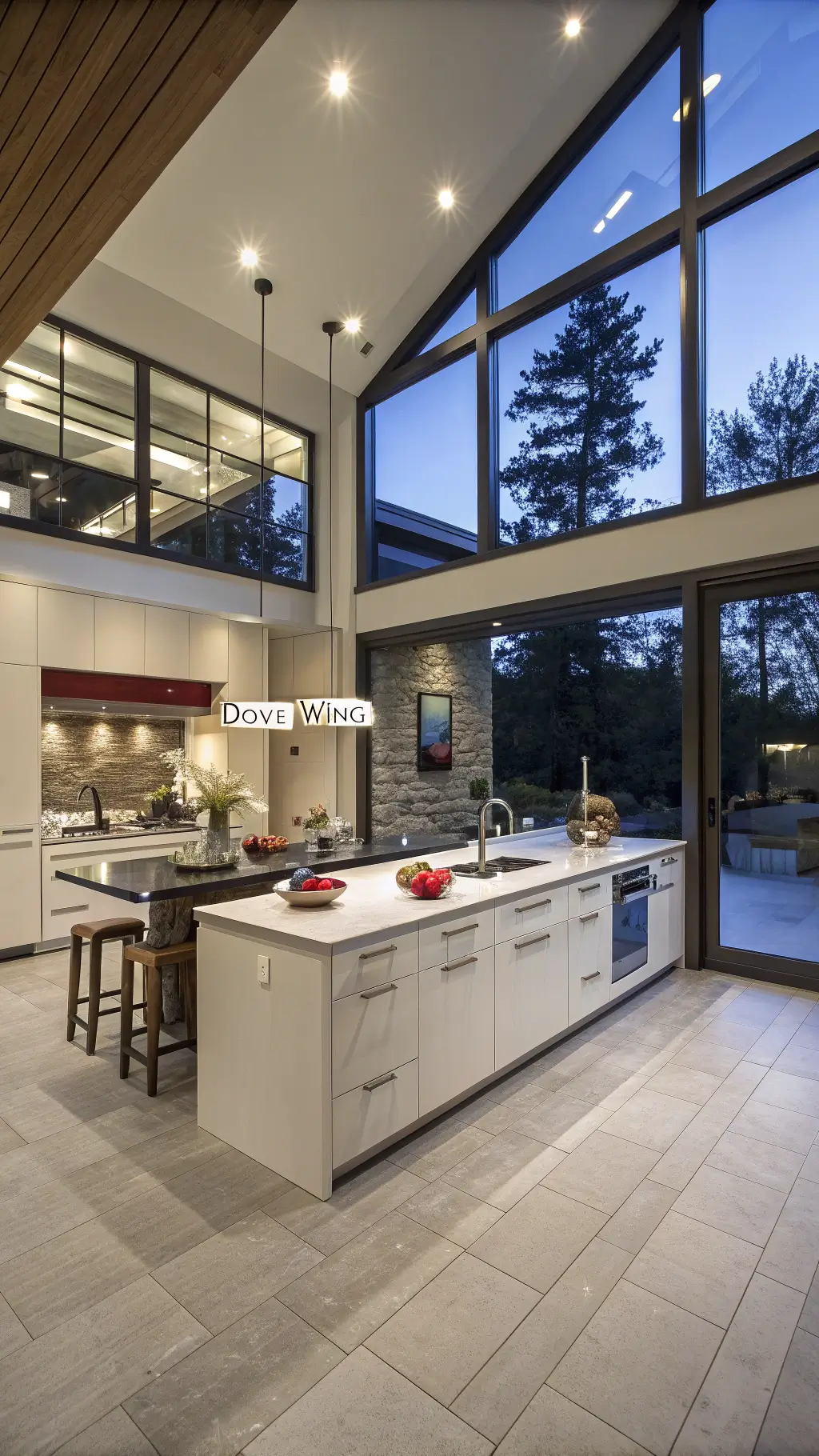 Contemporary open-concept kitchen with off-white flat-panel cabinets, dramatic clerestory windows, and a dark soapstone waterfall island, highlighted by blue hour and artificial lighting.