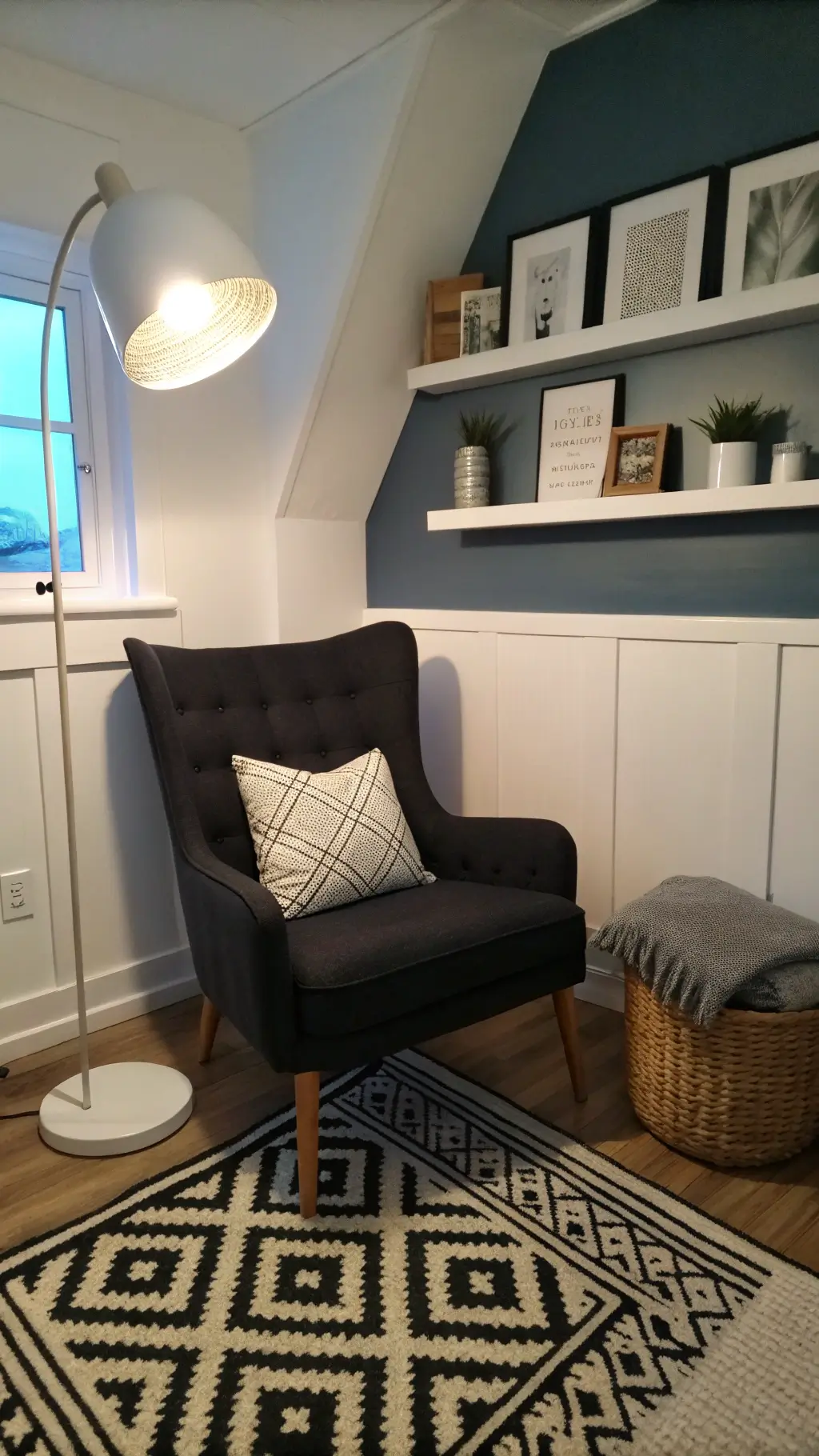 Cozy bedroom corner during blue hour with a black reading chair, white floor lamp, geometric rug, white floating shelf with monochrome art, and various textured accents.