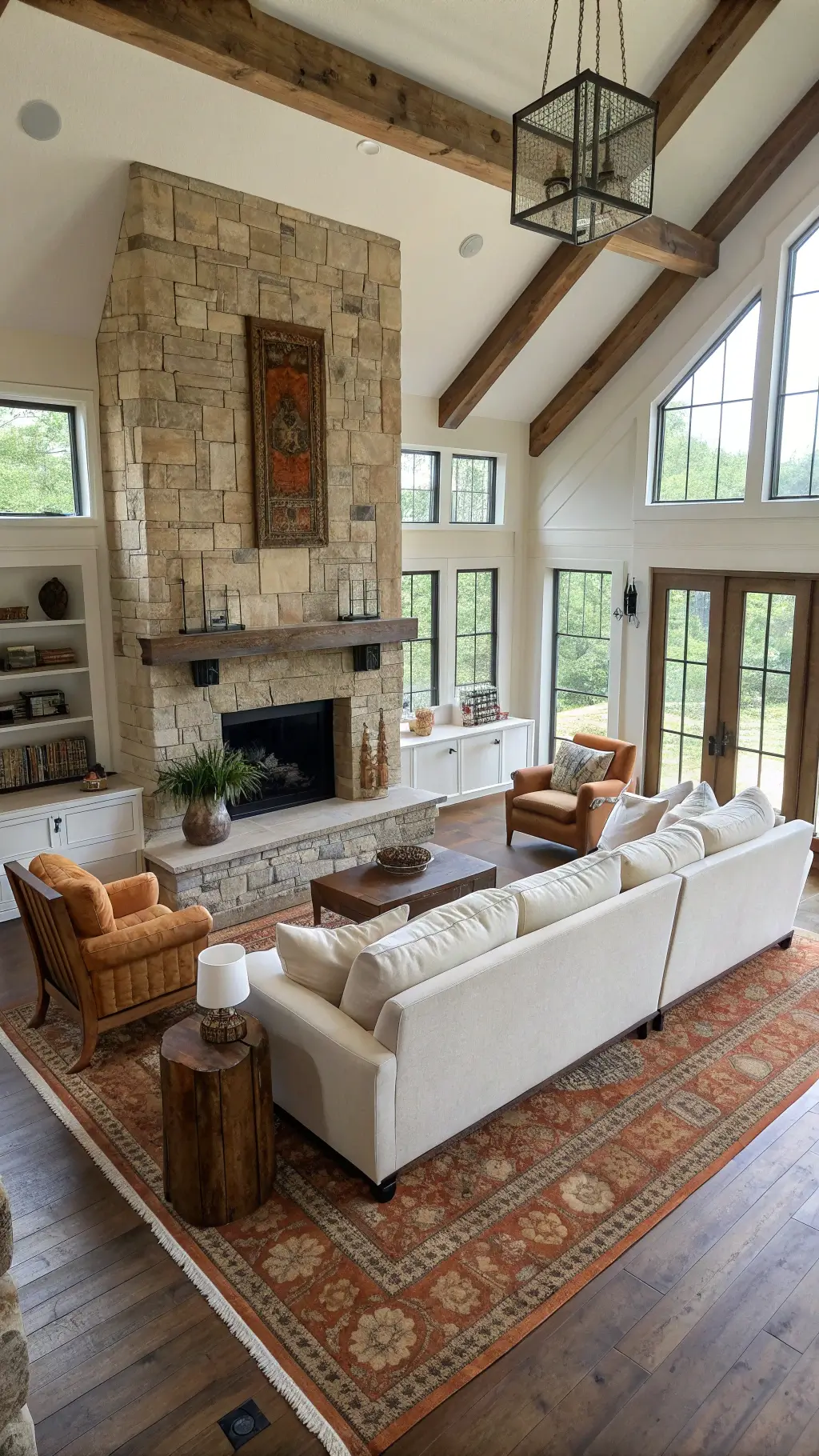 Open concept living room with large stone fireplace, ivory sectional, oak accent chairs, and vintage Turkish rug, brightly lit with natural light and iron sconces.