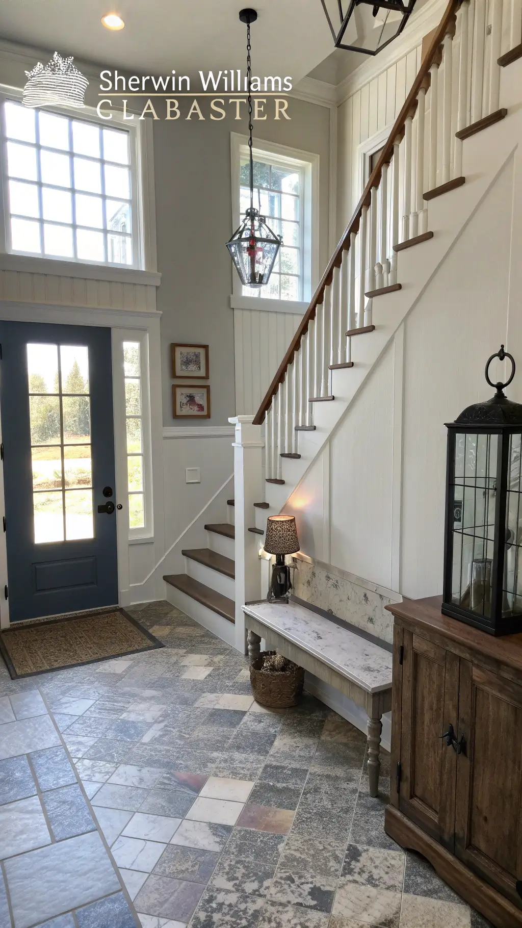Brightly lit farmhouse entry foyer featuring a statement staircase, vintage church bench, industrial coat hooks, mirror, slate tile flooring, vintage overdyed runner, iron and glass lantern pendant, and board and batten wall treatment painted in Sherwin Williams 'Alabaster'.