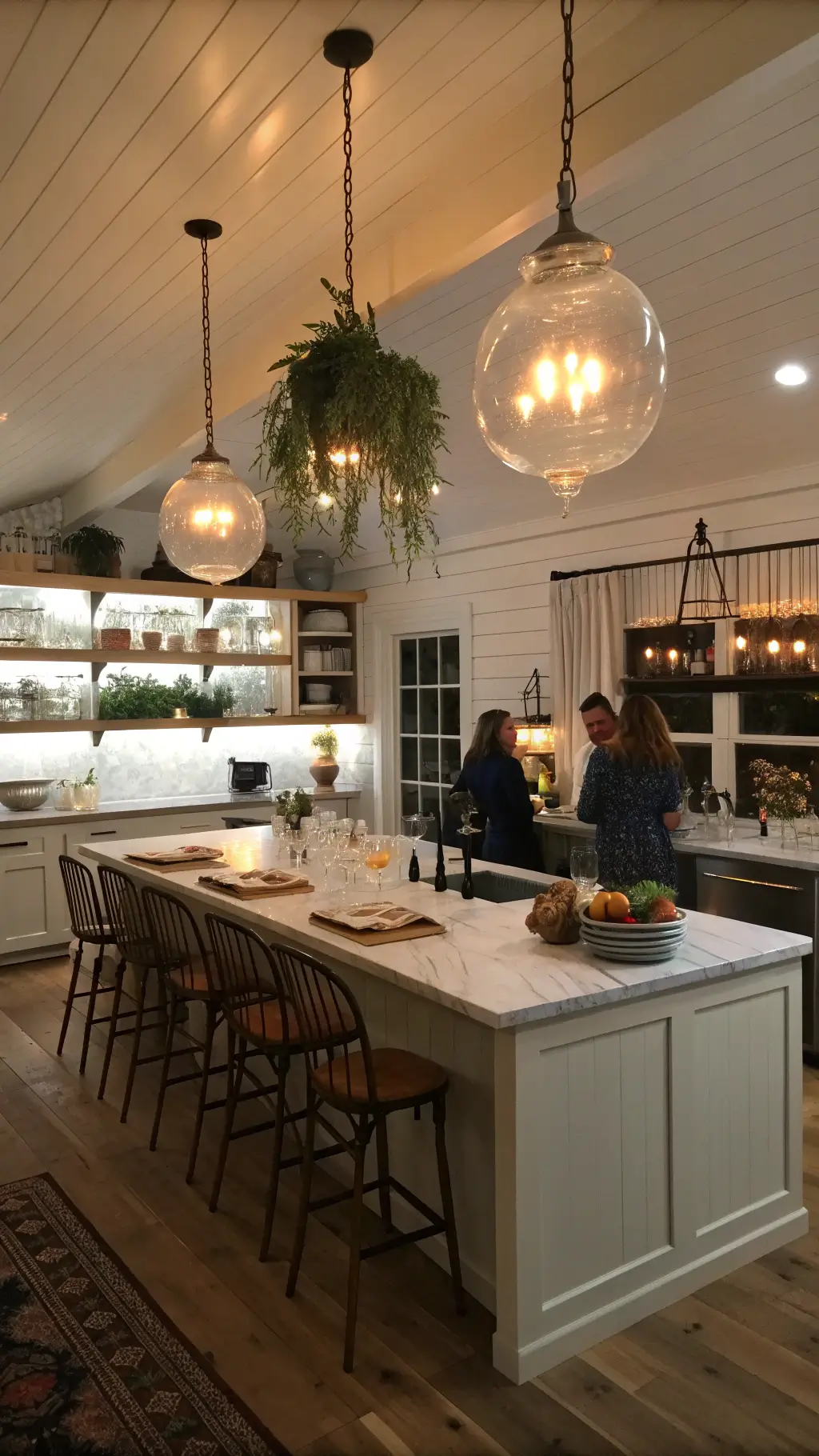 Evening kitchen scene with white marble island, open shelving, vintage runner on plank floors, shiplap walls, dried herbs, fresh greenery, and ambient lighting for social gathering